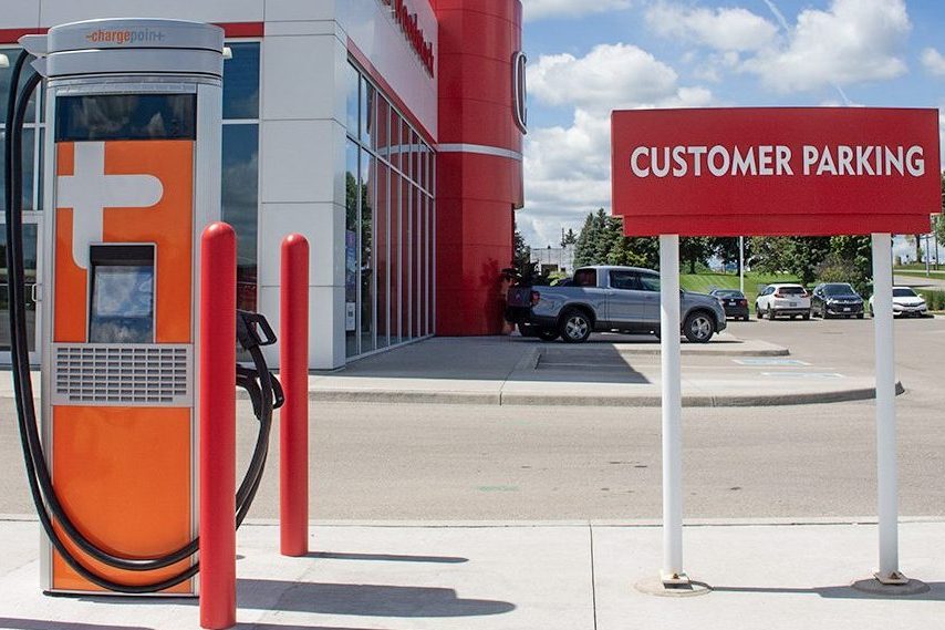 Electric vehicle charging station at a car dealership with the text 'Automotive Dealerships' inviting visitors to learn more about ChargerCrew's dealership services.